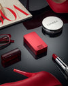 Designer Red metal pill box by Ikigai Cases called the Mission Pill Case. Lying with lipstick, glasses, and heels - all red.