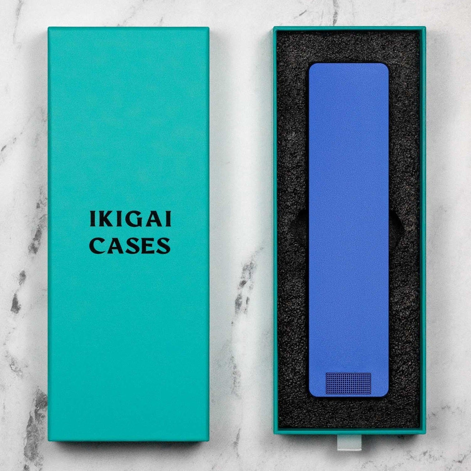 Teal-colored product box with 'IKIGAI CASES' text next to opened box revealing a pink phone case.