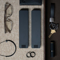 Two Matte Black Weekly Pill Cases laying next to glasses, keys, a wallet, rings, and lipstick.