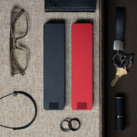 One Matte Black and one Designer Red Weekly Pill Cases laying next to glasses, keys, a wallet, rings, and lipstick.