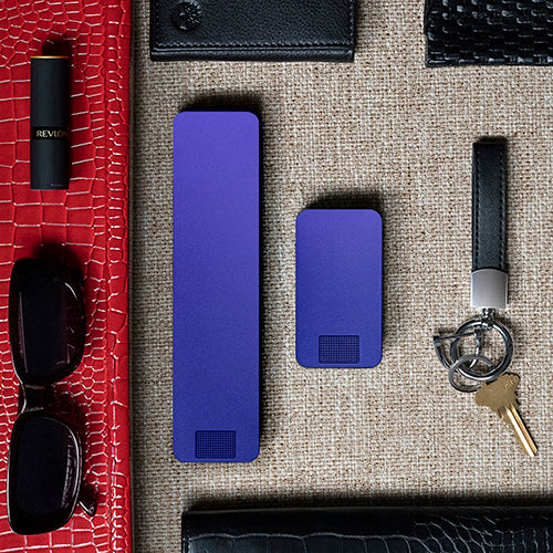 Everyday items including lipstick, keys, two smartphones, sunglasses, wallets, and a cord on an orange and beige background.