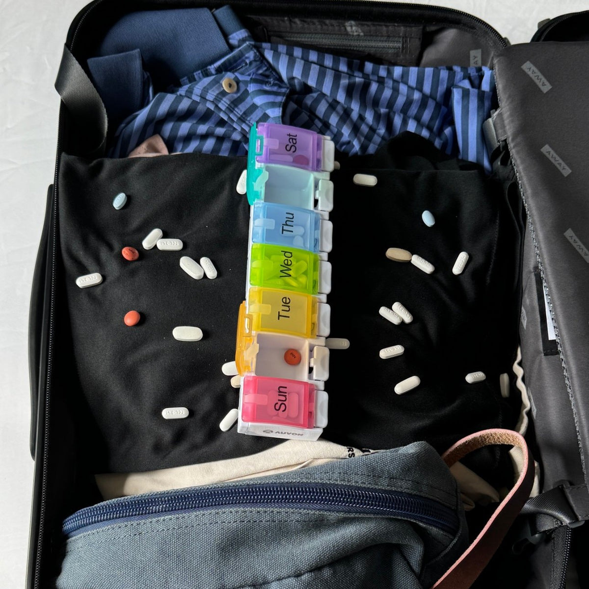 Plastic pill organizer popped open with pills spilled across a packed suitcase