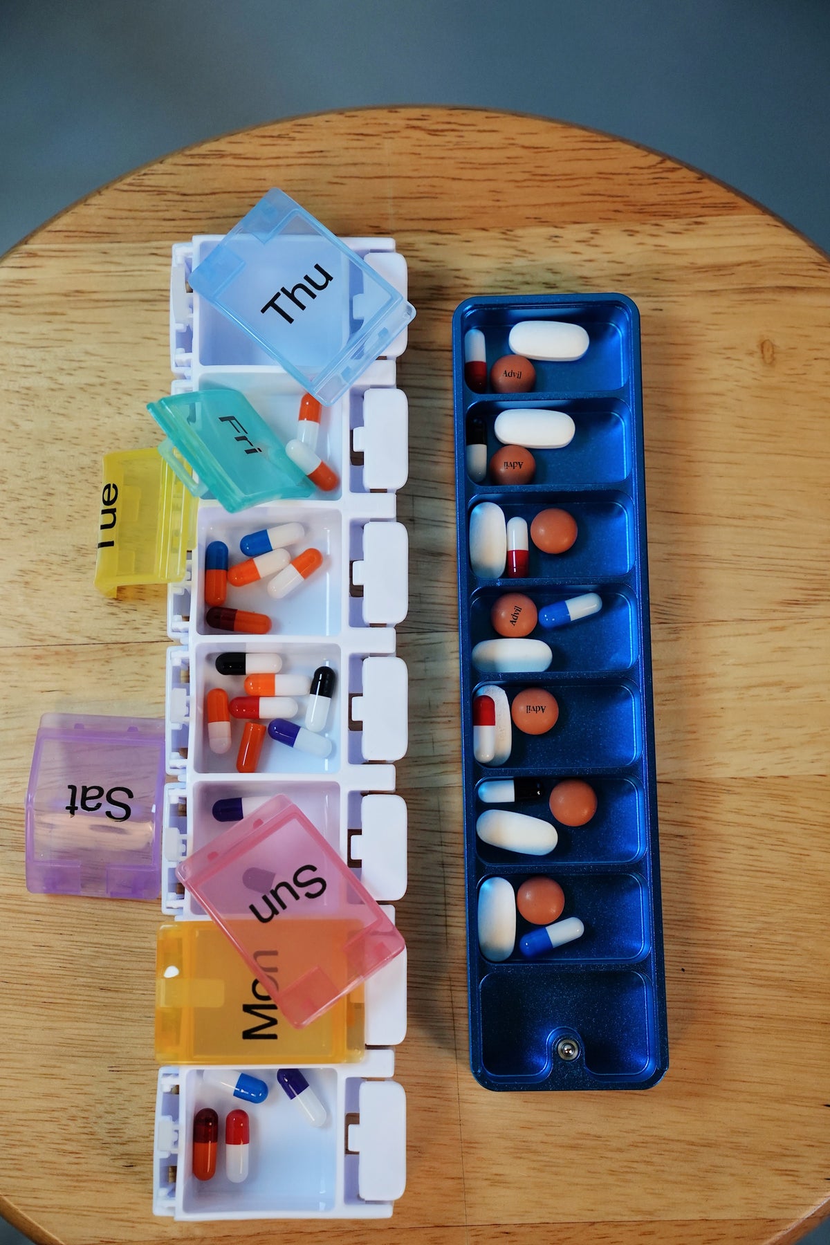 A plastic weekly pill organizer with lids hanging open next to an Ikigai aluminum case