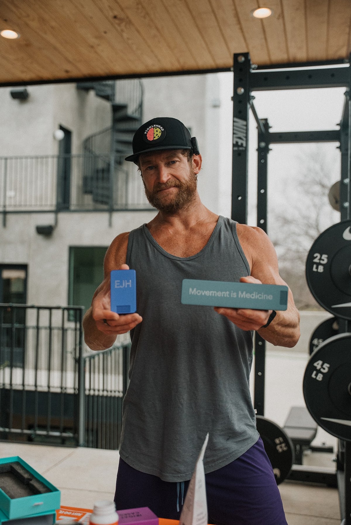 Eric Hinman in his home gym holding his EJH case and his Movement is Medicine case