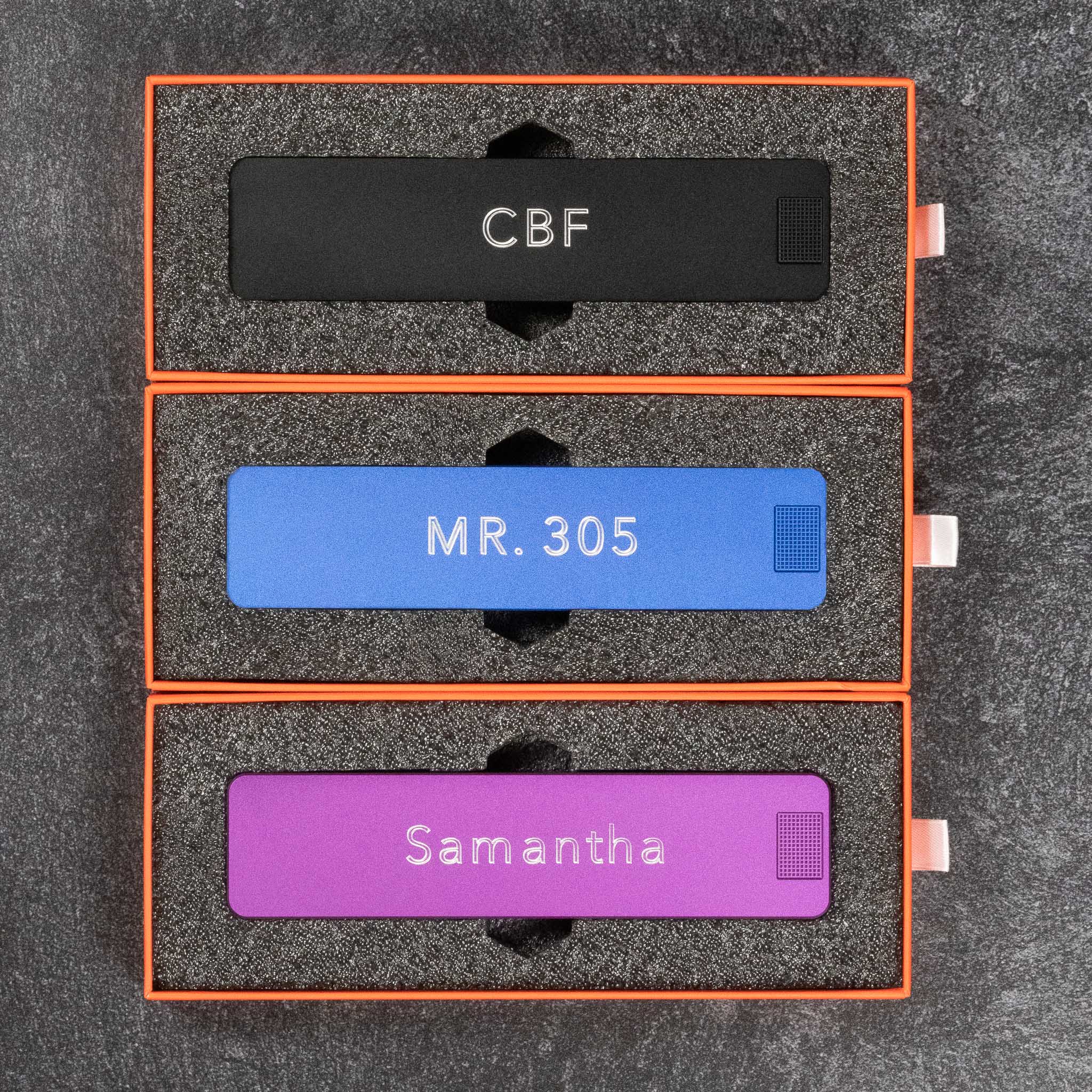 Three personalized nameplates in black, blue, and purple packaging.