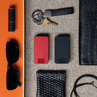 One Designer Red and One Matte Black Travel Pill Case laying next to a coin purse, women's sunglasses, lipstick, wallet and keys.
