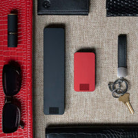 One Matte Black Weekly Pill Case and One Designer Red Travel Pill Case laying next to items for a ladies purse.