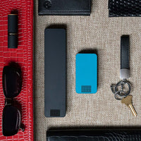One Matte Black Weekly Pill Case and One Bahama Blue Travel Pill Case laying next to items for a ladies purse.
