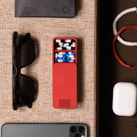 Red pill case with two compartments open. The compartments are full of pills. There is an IPhone, Airpods, A Wallet, and Sunglasses.